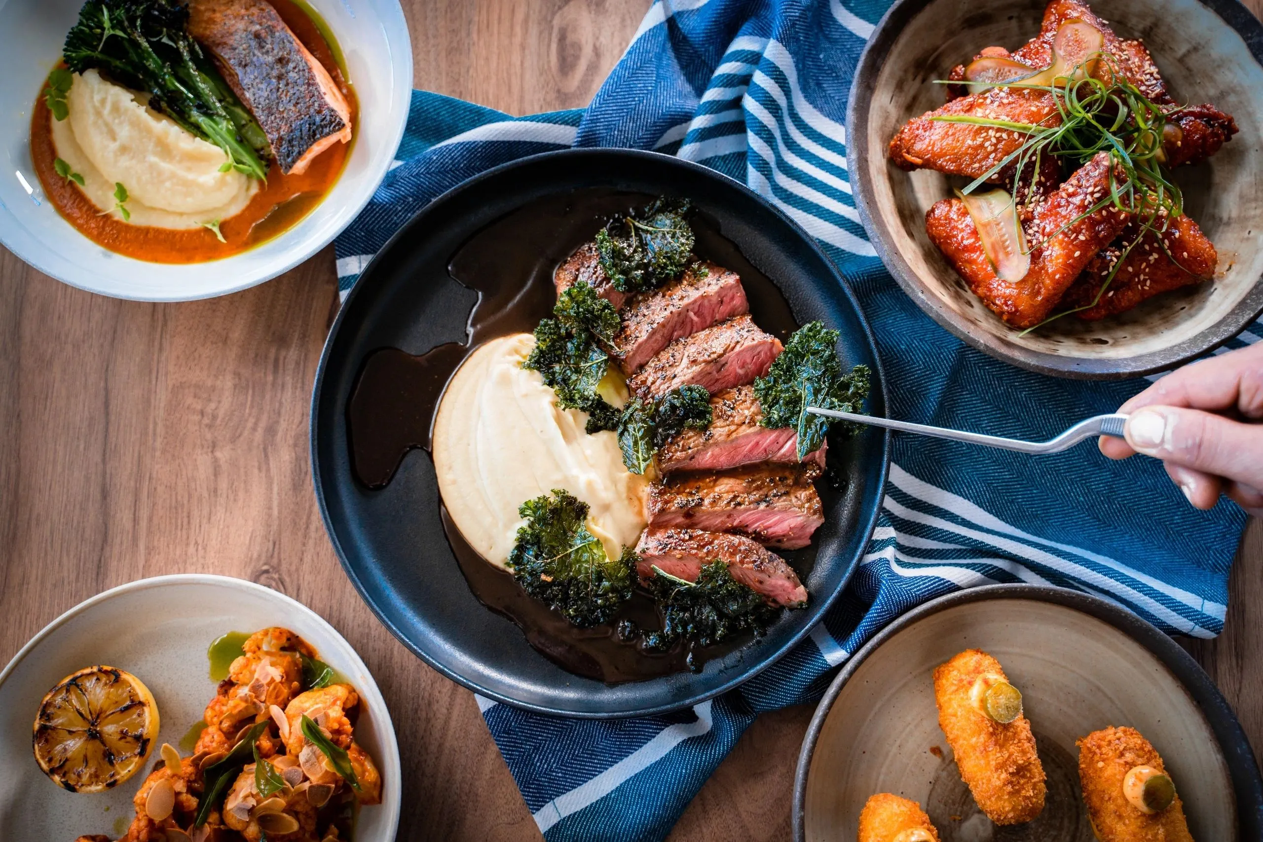 Sliced steak on mash being served from above, surrounded by share plates