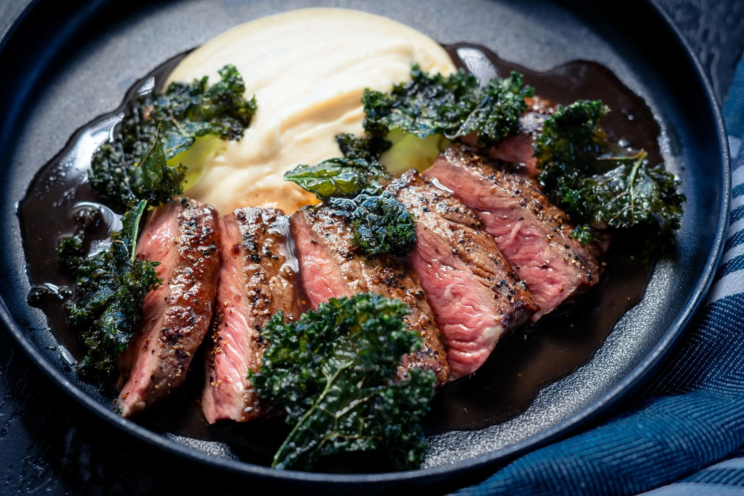 Sliced steak, crisp kale and creamy mash in a dark bowl